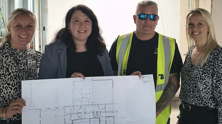 Photograph of four people holding an architectural drawing